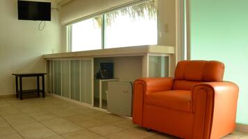 Una habitación con un ventanal grande, un televisor en la pared, una mesita pequeña y una silla naranja.