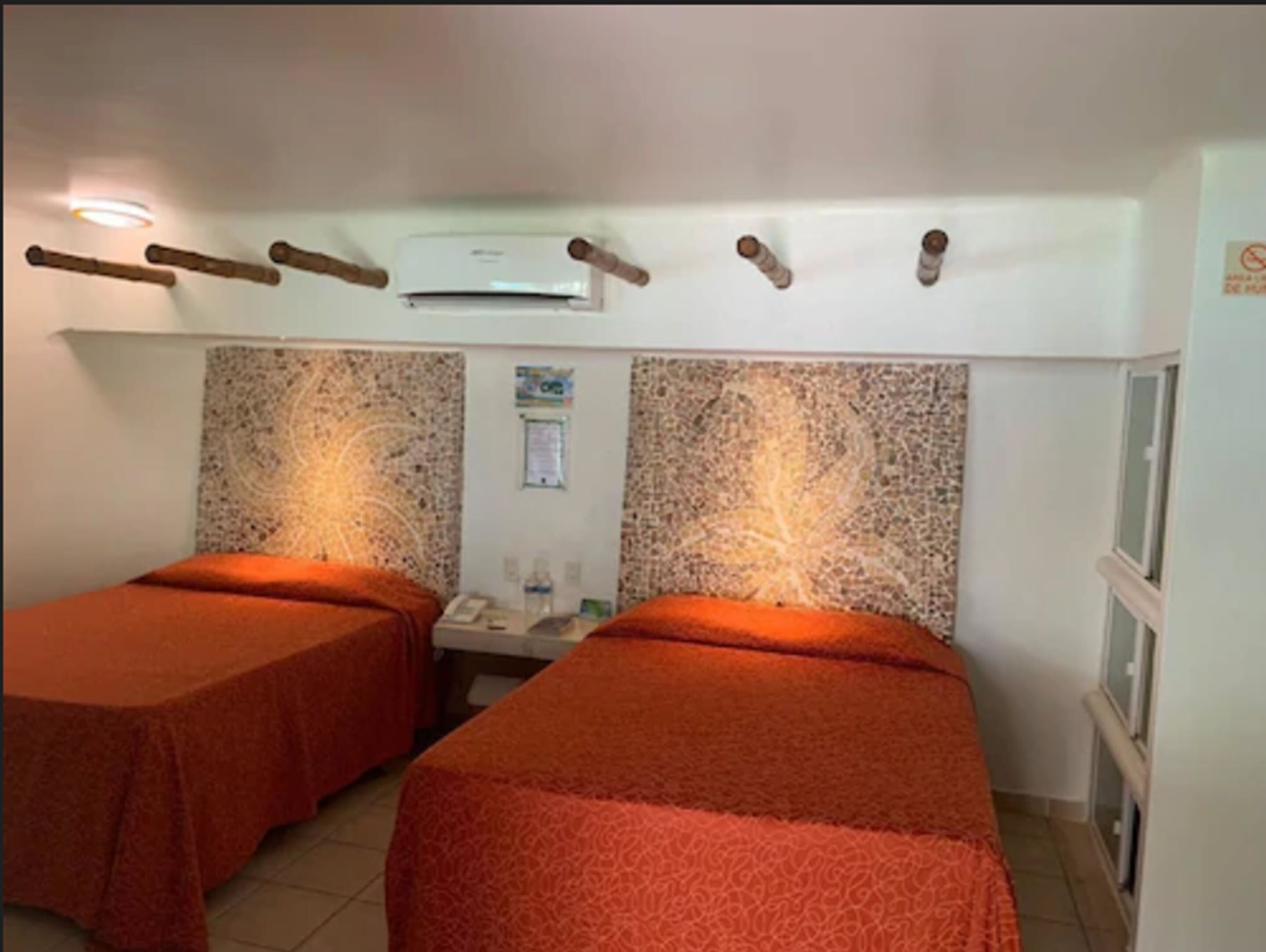 A room with two beds, a small table, a wall-mounted air conditioner, and a poster on the wall.