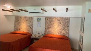 Una habitación con dos camas, una mesita pequeña, aire acondicionado de pared y un cartel en la pared.