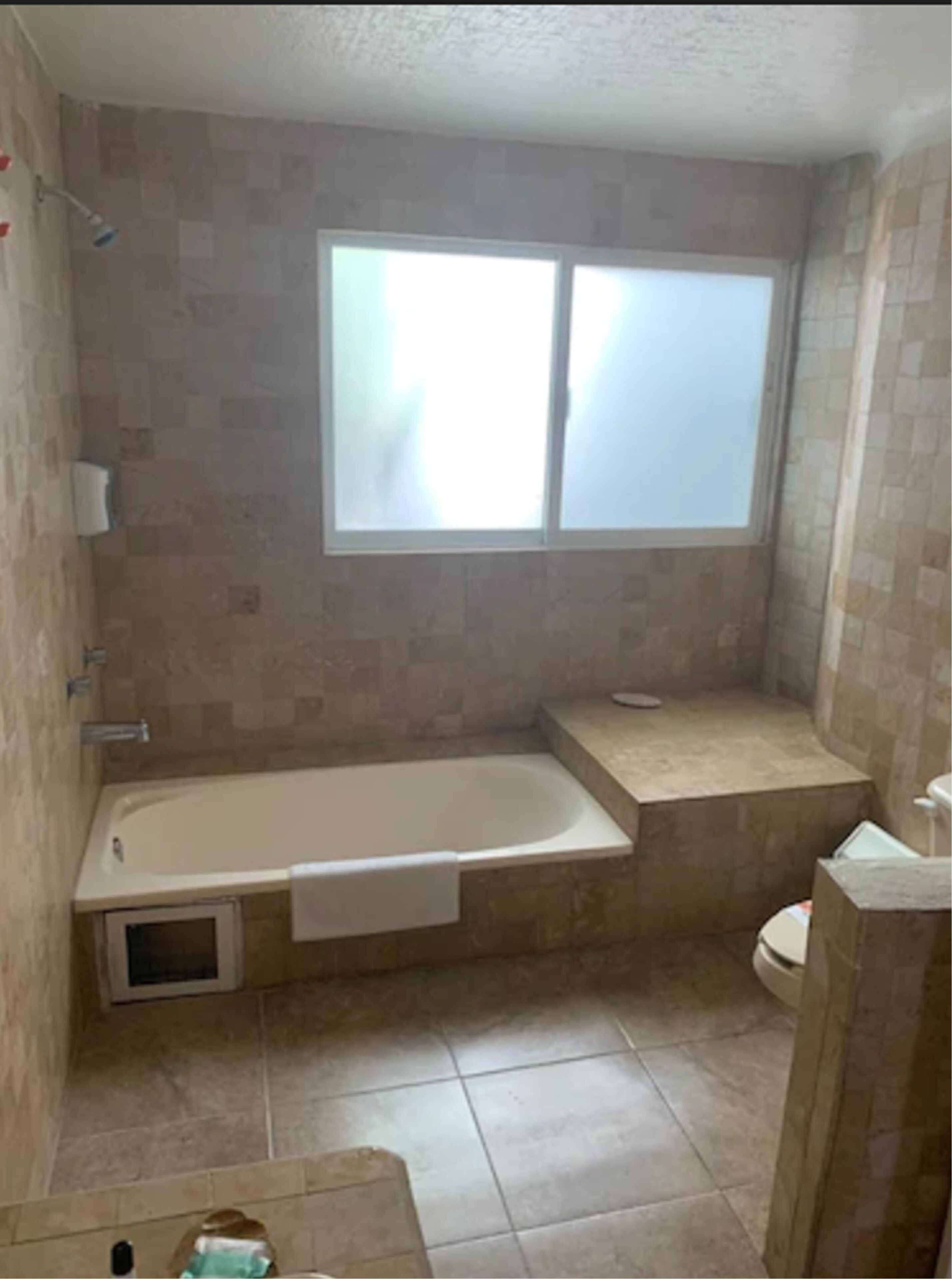 A bathroom with a bathtub, a window, and a toilet.