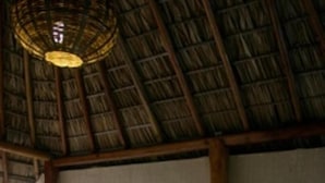 A room with a thatched roof, a sofa with patterned cushions, a glass table with a bowl of stones, and a wooden chair. - Hotel Paraiso Escondido (Puerto Escondido)
