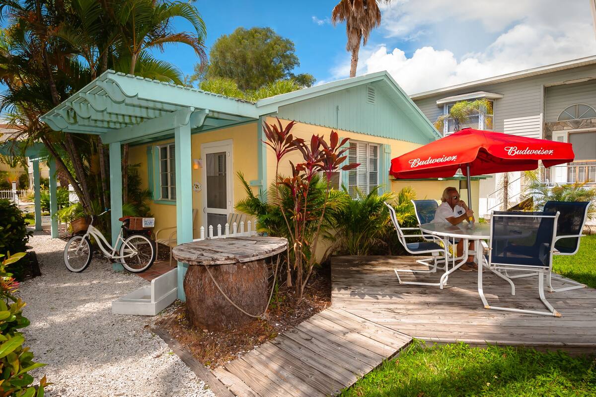 Een klein huis met een veranda, een fiets en een tafel met stoelen.