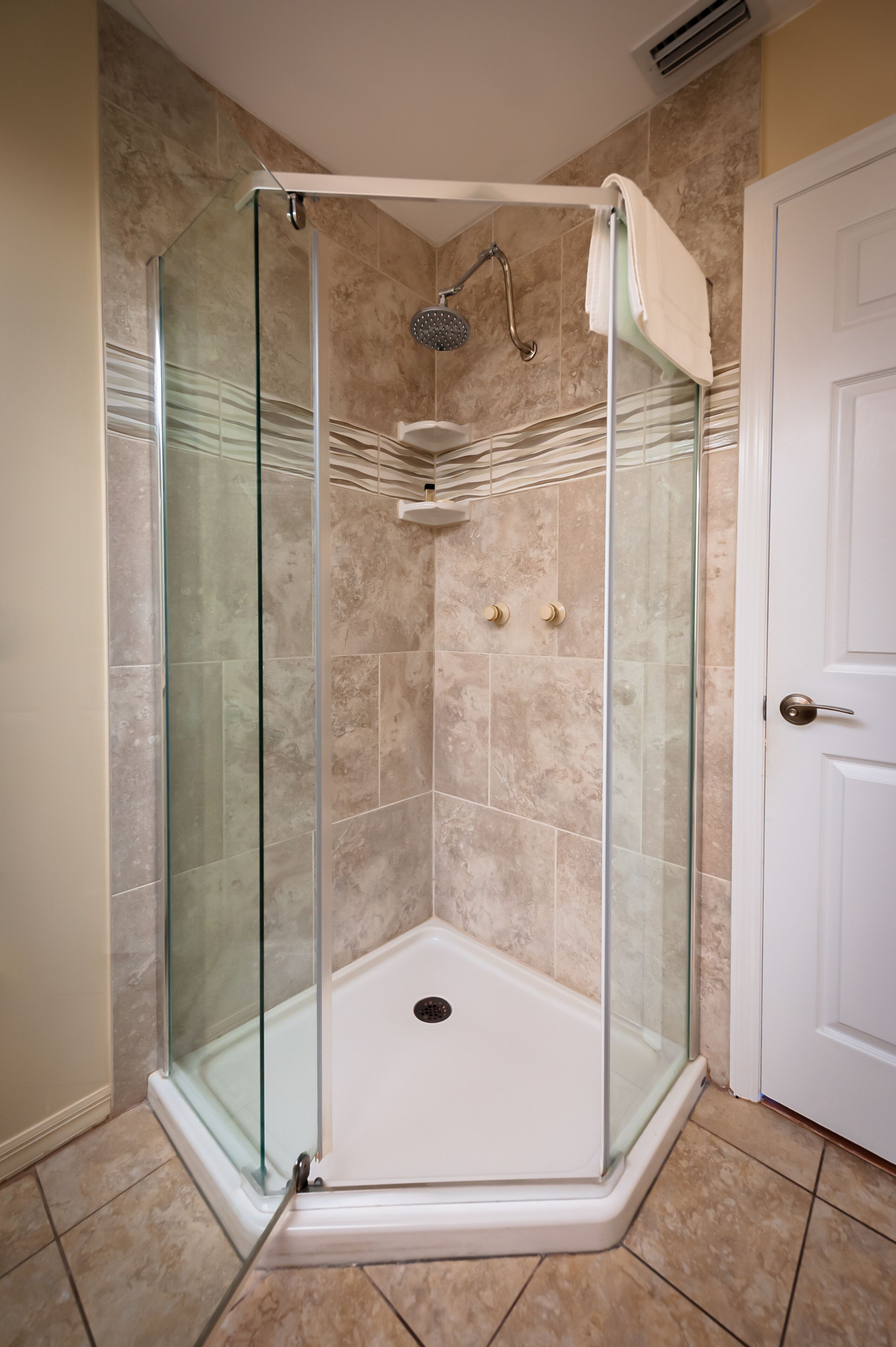 A glass-enclosed shower stall with a white door, beige tiled walls, and a white door frame.