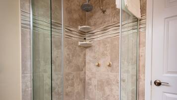 A glass-enclosed shower stall with a white door, beige tiled walls, and a white door frame.