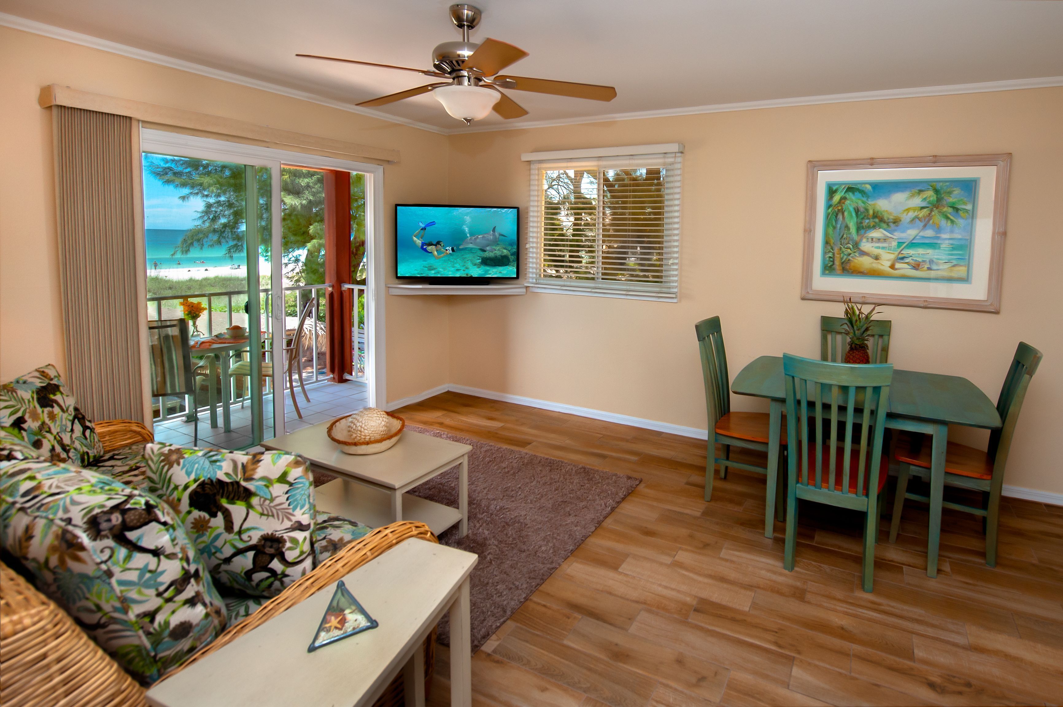 A living room with a television, a dining table with chairs, a sofa, and a view of the beach through the sliding doors.
