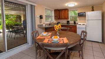 A kitchen with a dining table set for two, a stove, microwave, and refrigerator.