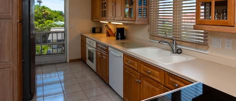 A kitchen with wooden cabinets, a dishwasher, a coffee maker, and a window with blinds.