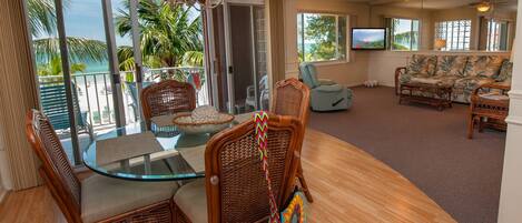 A spacious living room with a glass table, wicker chairs, a sofa, and a television.