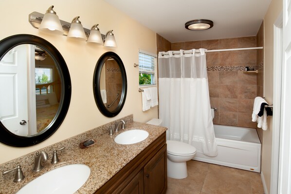 A bathroom with a double sink vanity, a toilet, a bathtub, and a shower curtain.