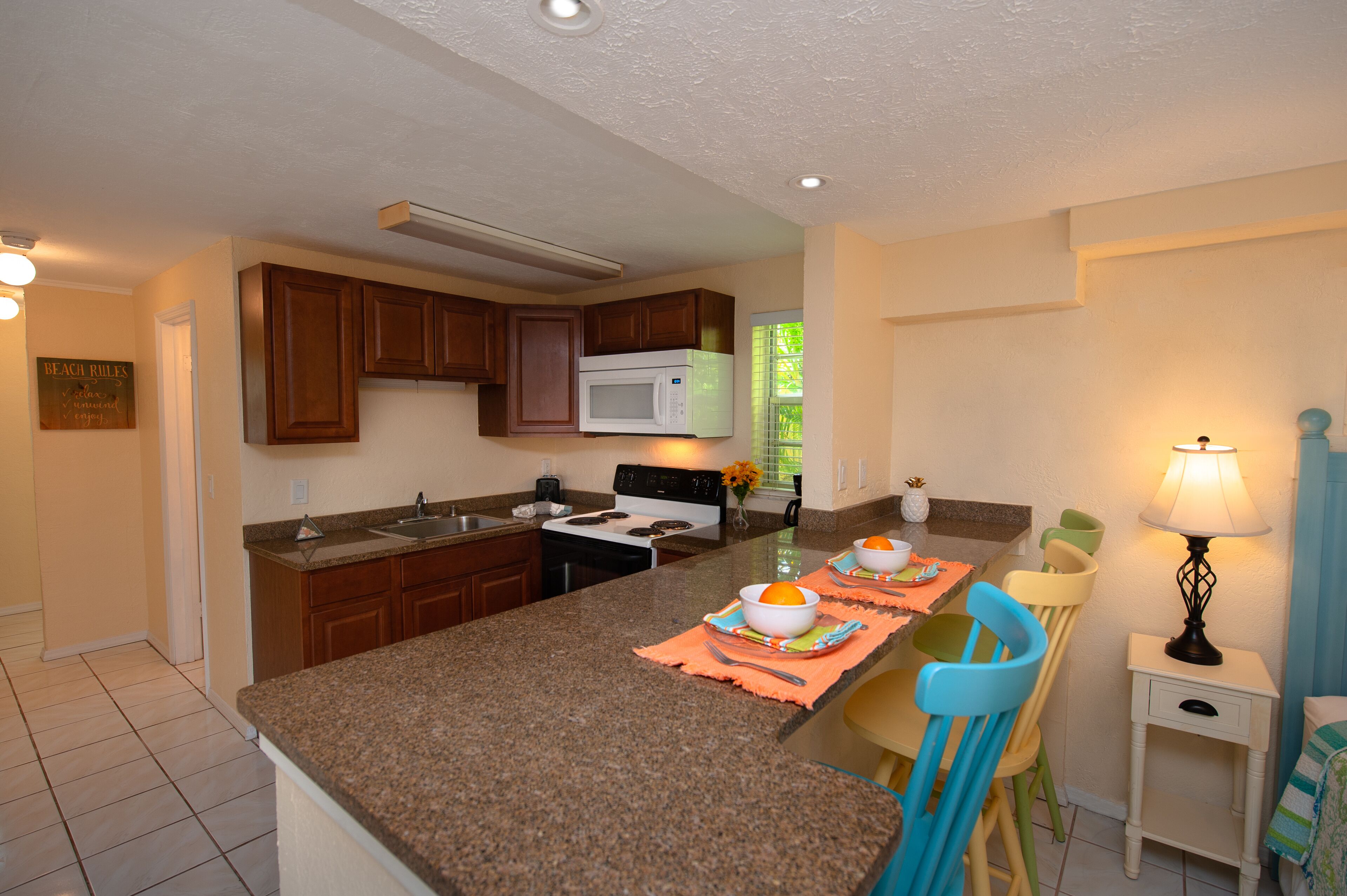 A kitchen with granite countertops, wooden cabinets, a microwave, stove, and a dining area with chairs and a table set for two.
