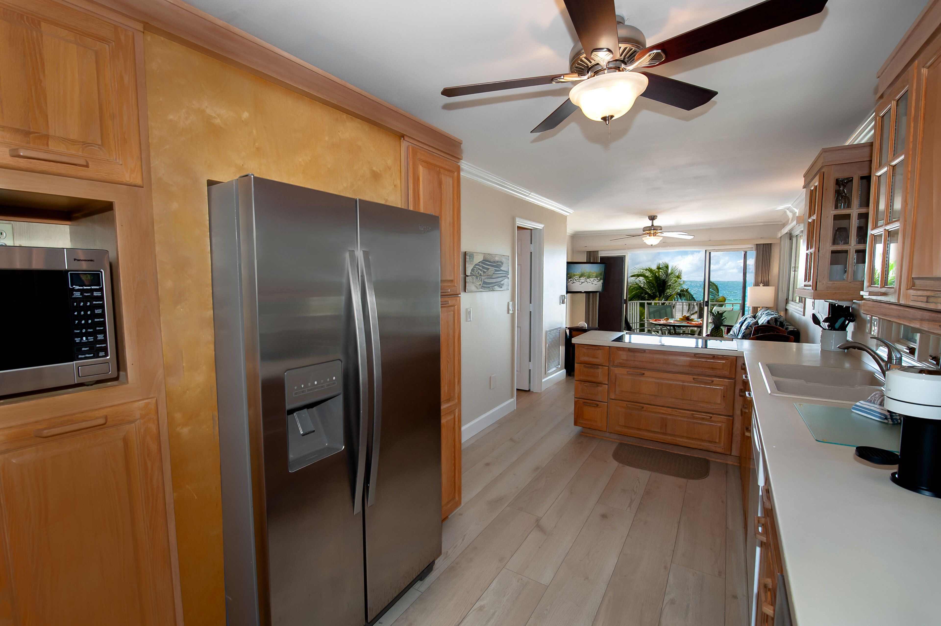 A modern kitchen with wooden cabinets, a stainless steel refrigerator, a microwave, and a ceiling fan.