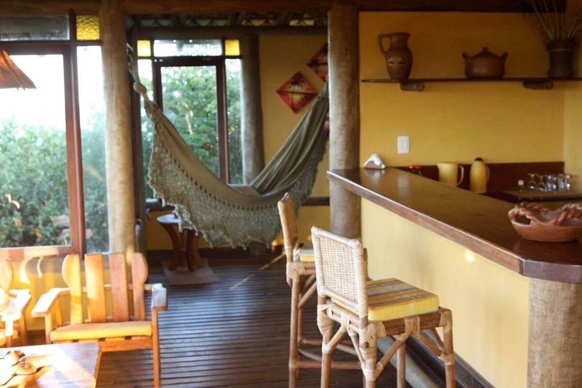 Une terrasse en bois avec des chaises en osier, un hamac et un coin bar équipé de tabourets.