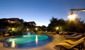 A swimming pool with lounge chairs and umbrellas, surrounded by buildings and trees.