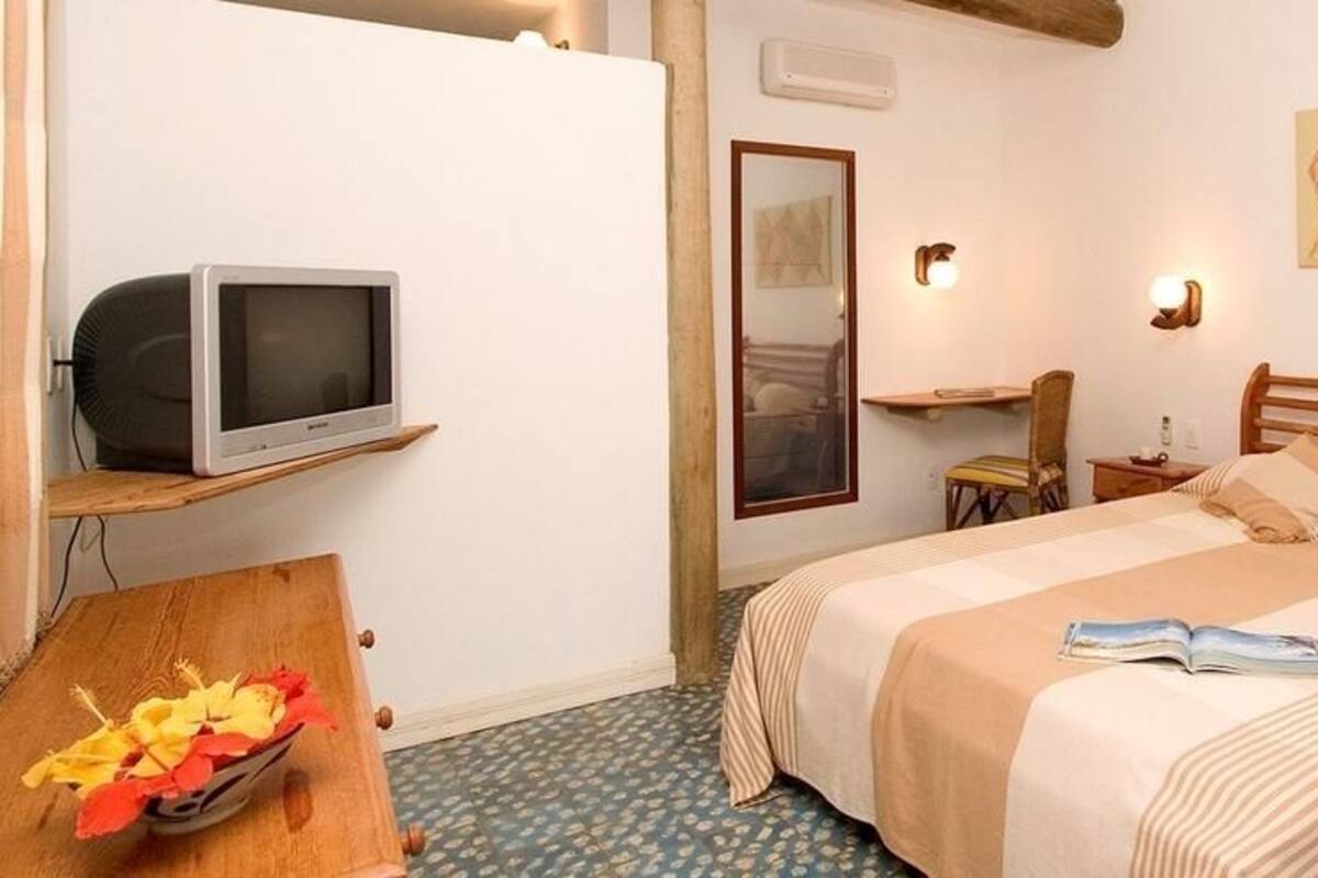 Une chambre d’hôtel avec un lit, un téléviseur posé sur une étagère, un bureau avec une chaise et un tableau accroché au mur.