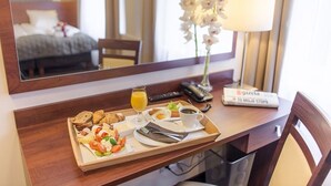 A breakfast tray with croissants, eggs, tomatoes, and juice on a wooden desk with a mirror, a lamp, and a sign in a hotel room. - City Center Rooms (Lodz)