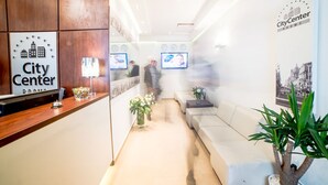 A reception area with a wooden reception desk, a white sofa, and a plant. - City Center Rooms (Lodz)