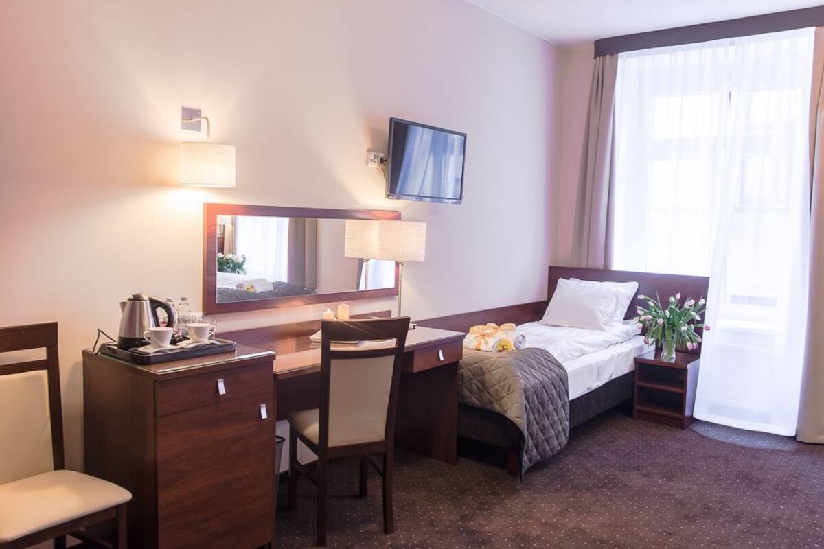 Ein Hotelzimmer mit Bett, Schreibtisch mit Stuhl, Fernseher, Spiegel und einem fenster mit Vorhängen.