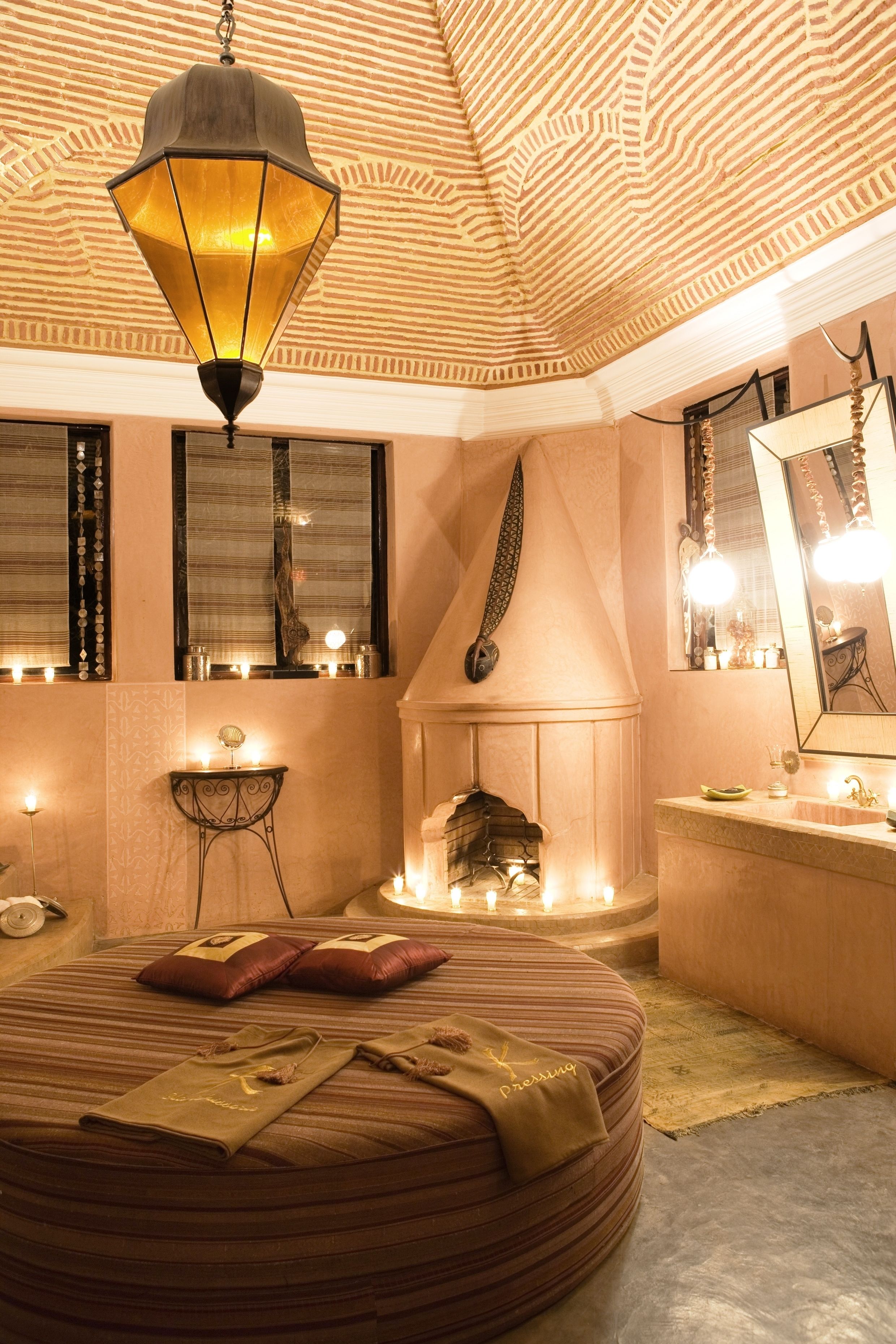 A room with a round bed, a fireplace, and a large mirror.