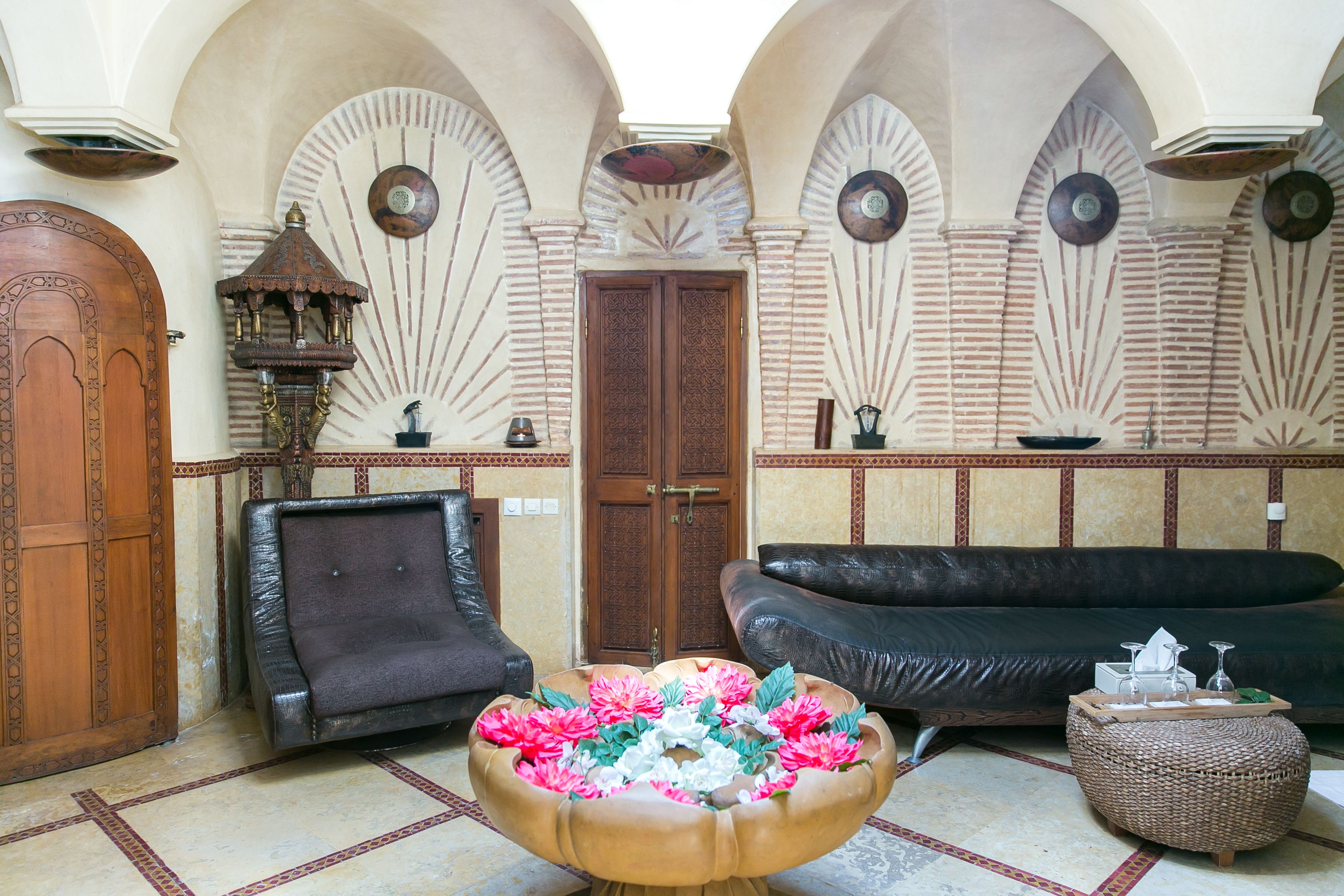 Eine Lobby mit einer Holztür, einem schwarzen Ledersofa, einem Dekorationstisch mit Blumen und einer Wand mit Erkerfenstern.