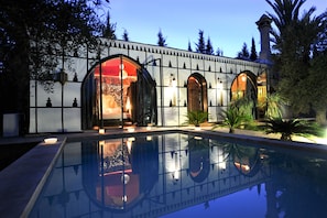 Vista de la piscina con un edificio de aberturas arqueadas y su reflejo en el agua.