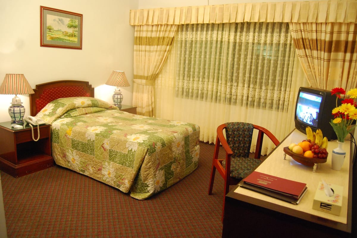 Une chambre d’hôtel comprenant un lit, un bureau avec un ordinateur, une chaise, un téléphone, une télévision et une fenêtre avec des rideaux.