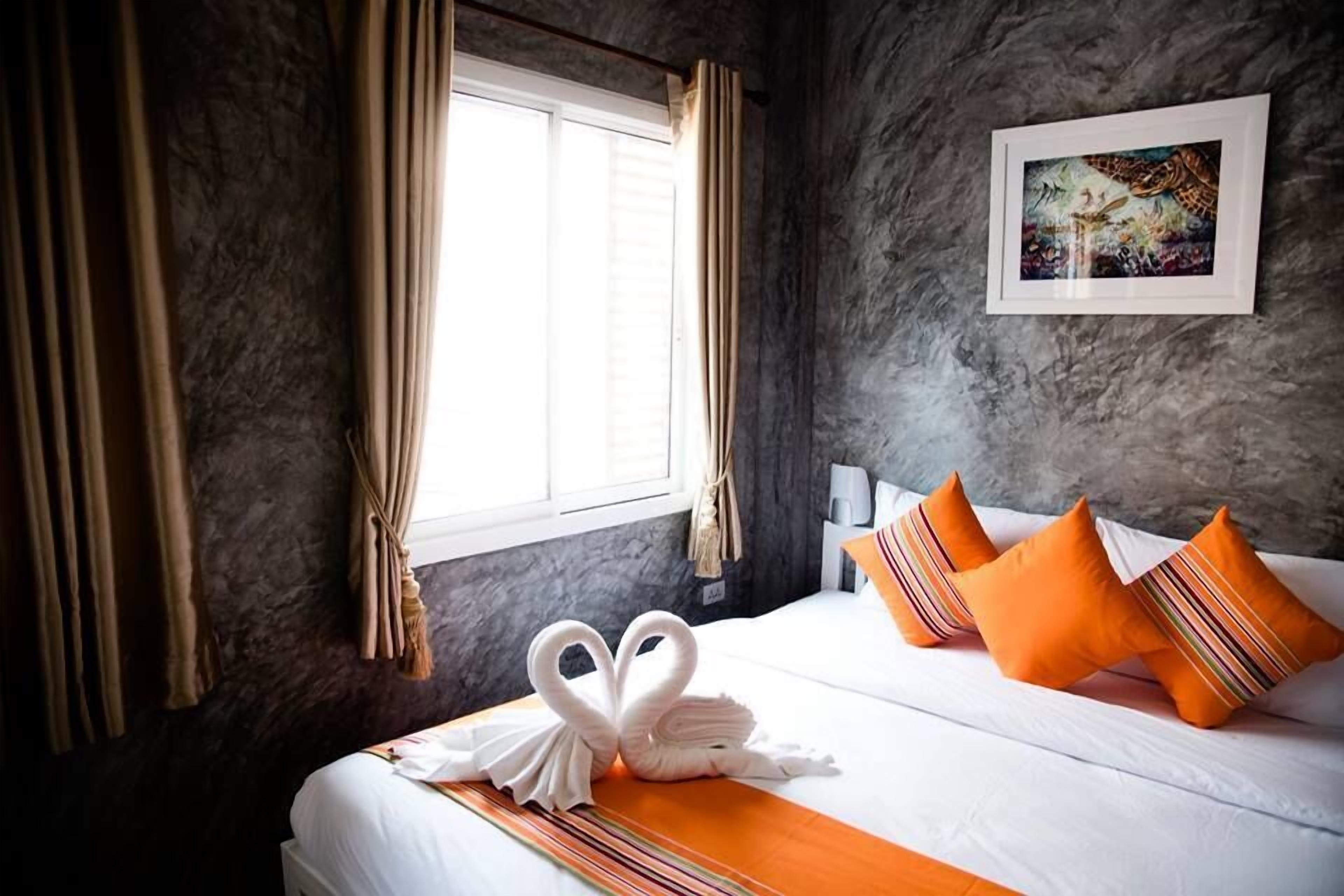 A hotel room with a bed, curtains, a framed picture on the wall, and a swan-shaped towel on the bed.