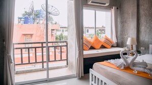 Een hotelkamer met balkon, een bed met oranje kussens, een lamp en een handdoekfiguur van een zwaan.