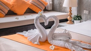 Een hotelkamer met een bed, een raam met oranje kussens, een lamp en een decoratieve zwaan van handdoeken.