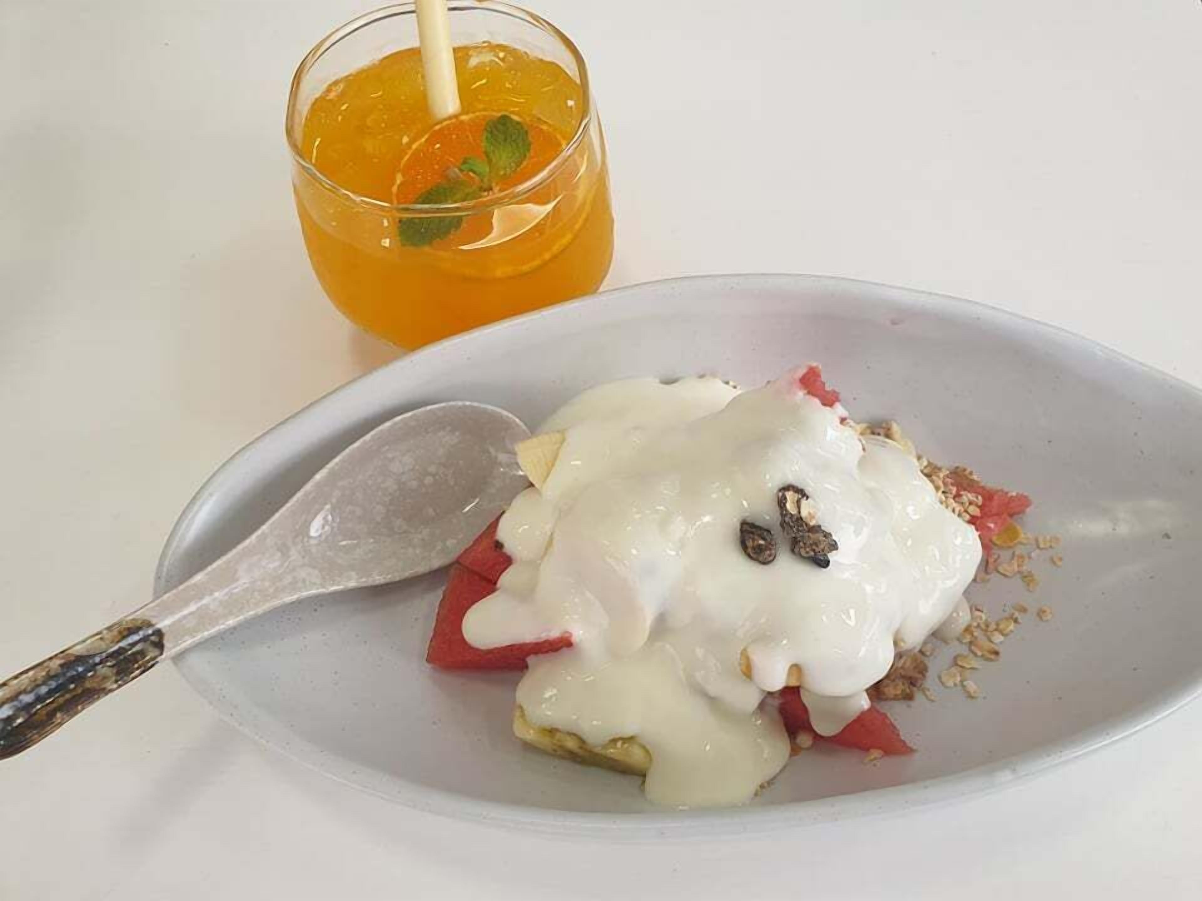 Un plato con postre, una bola de helado cubierta con crema blanca y nueces, acompañado de un vaso de jugo de naranja con una ramita de menta.
