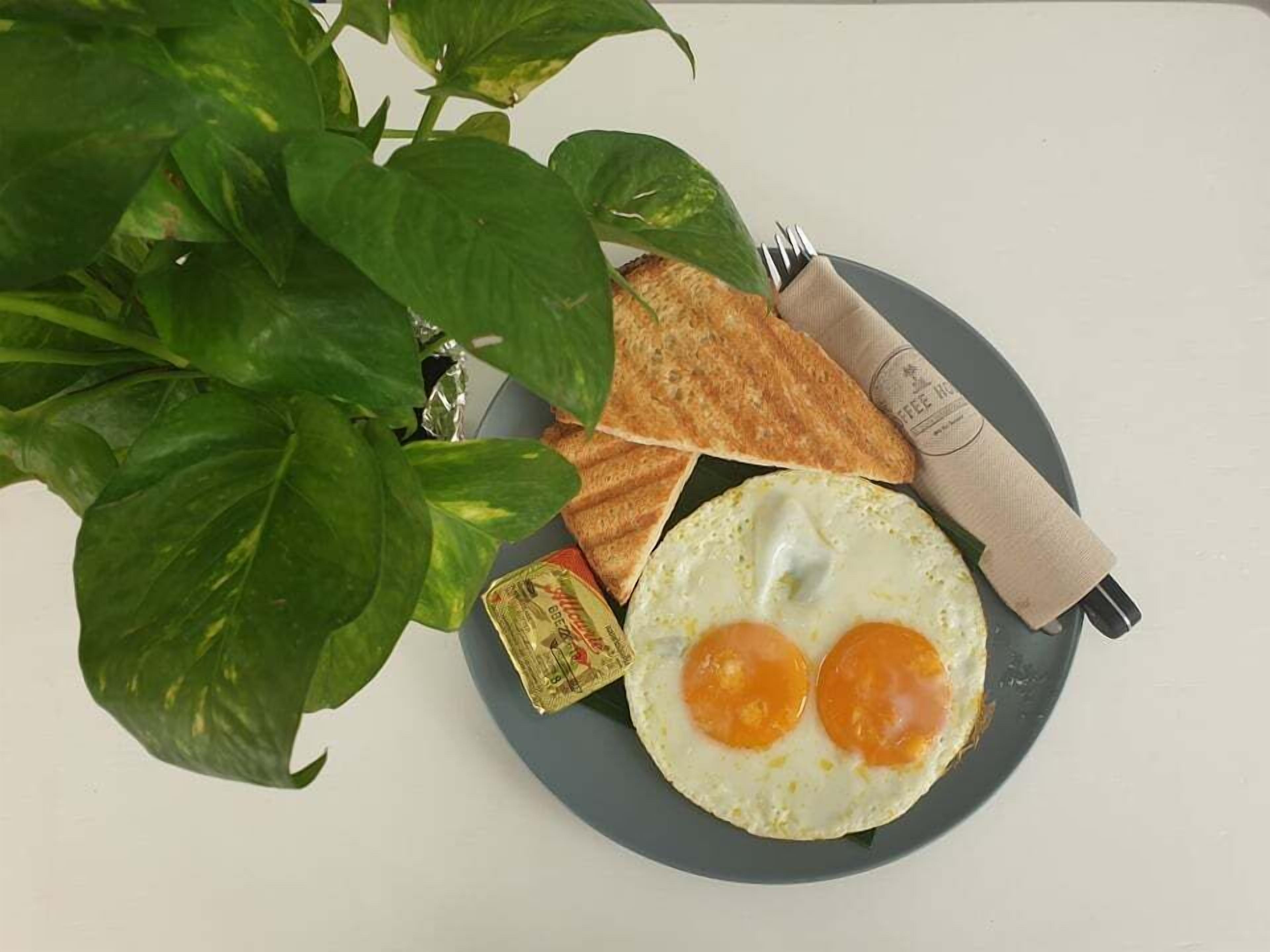 A plate with two fried eggs, a slice of toast, and a small packet of butter on a grey plate.