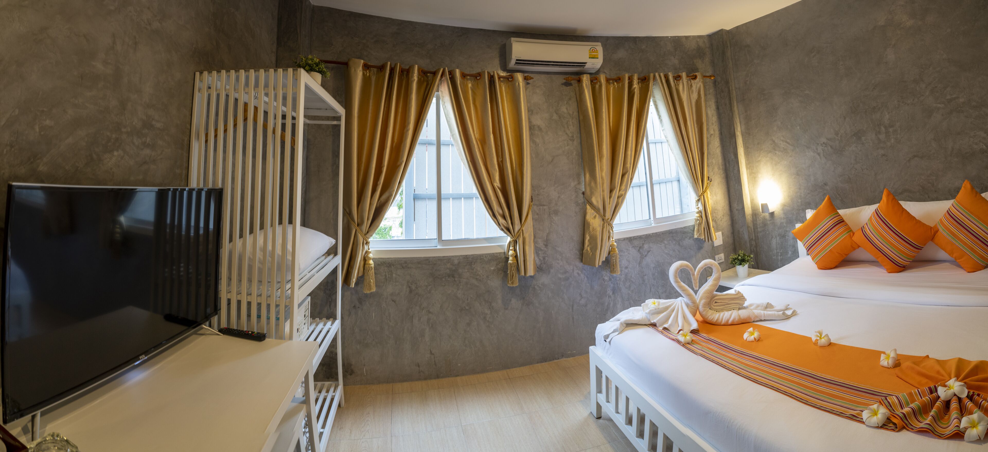 A hotel room with a bed, a TV, a window with curtains, and an air conditioning unit.