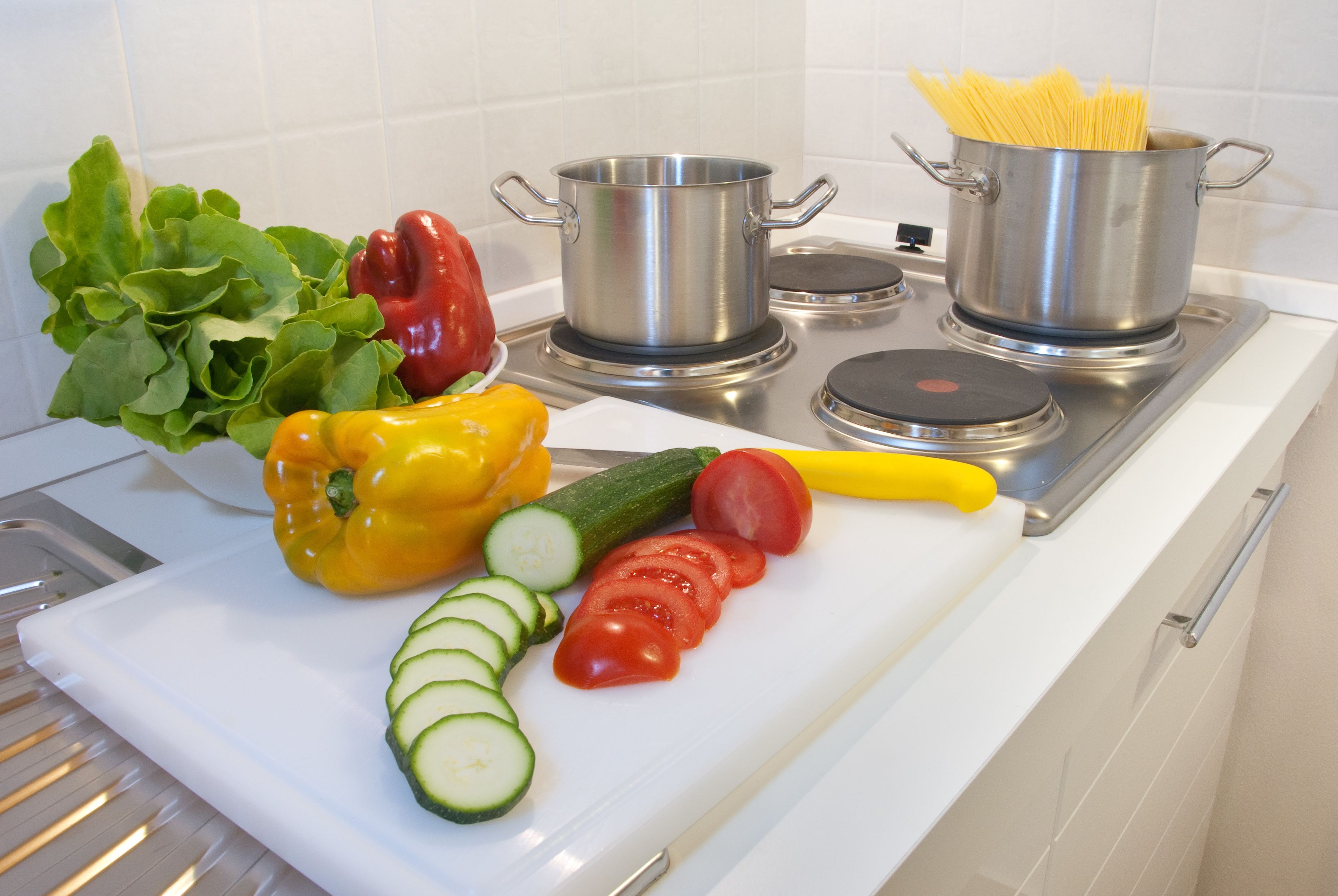 A kitchen with a cutting board, vegetables, and pots on the stove.
