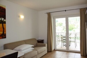 Una habitación con sofá, una mesita, una lámpara de pared y una puerta corrediza de vidrio que da a un espacio exterior con sillas.