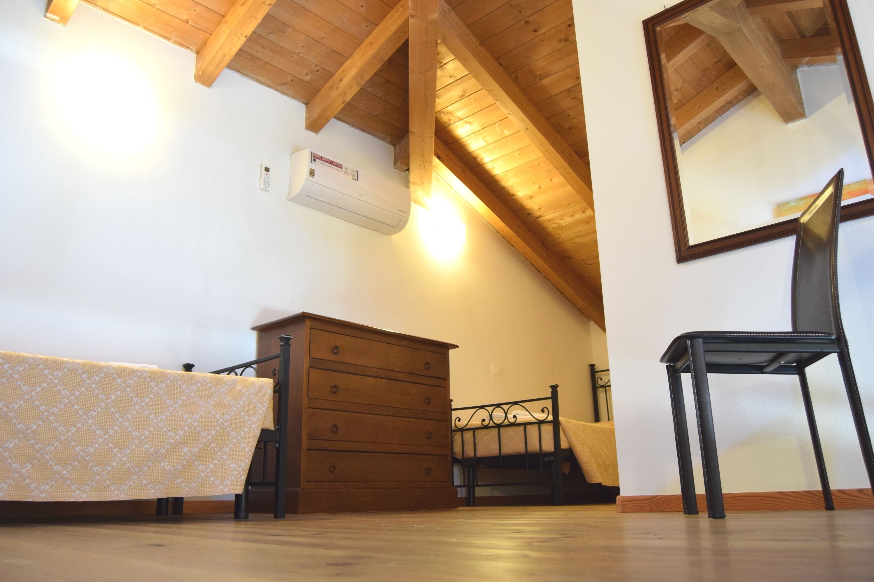 Un dormitorio con techo de madera, una cama con colcha estampada, un aparador, una silla y un espejo.