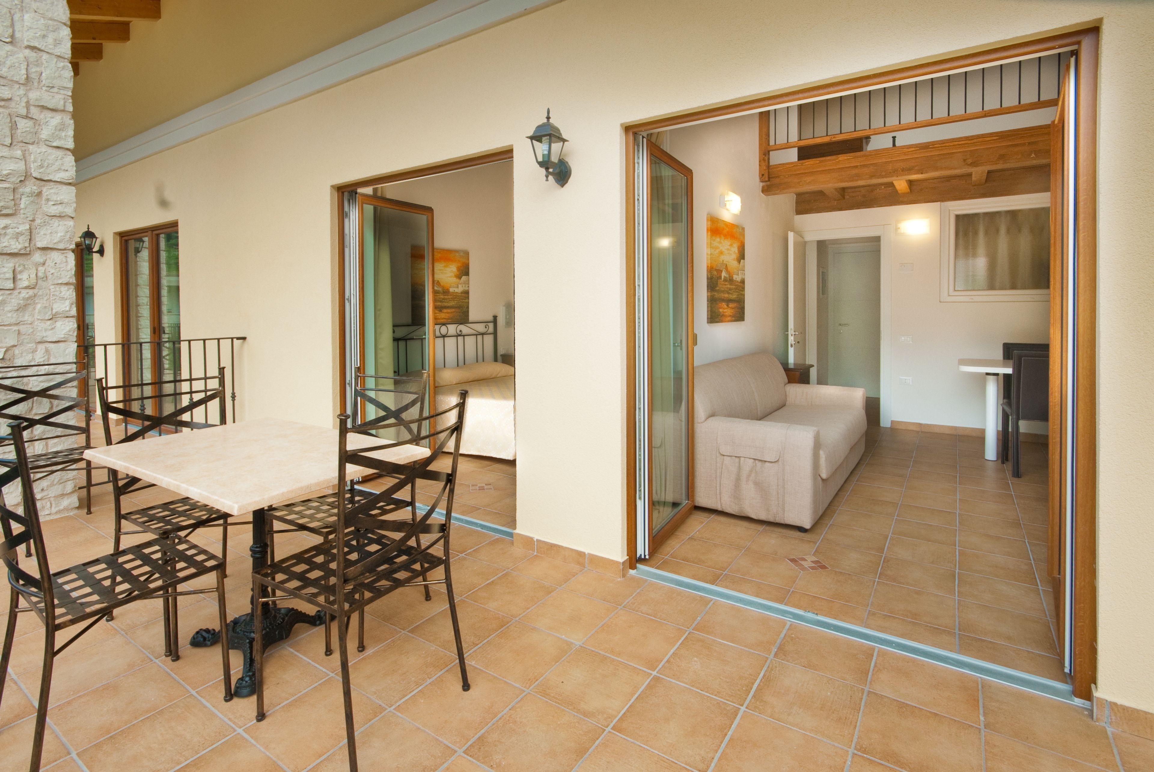 A spacious living area with a tiled floor, a dining table with chairs, a sofa, and a glass door leading to another room.