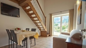 A dining area with a table set for four, a wooden staircase, and a sofa.