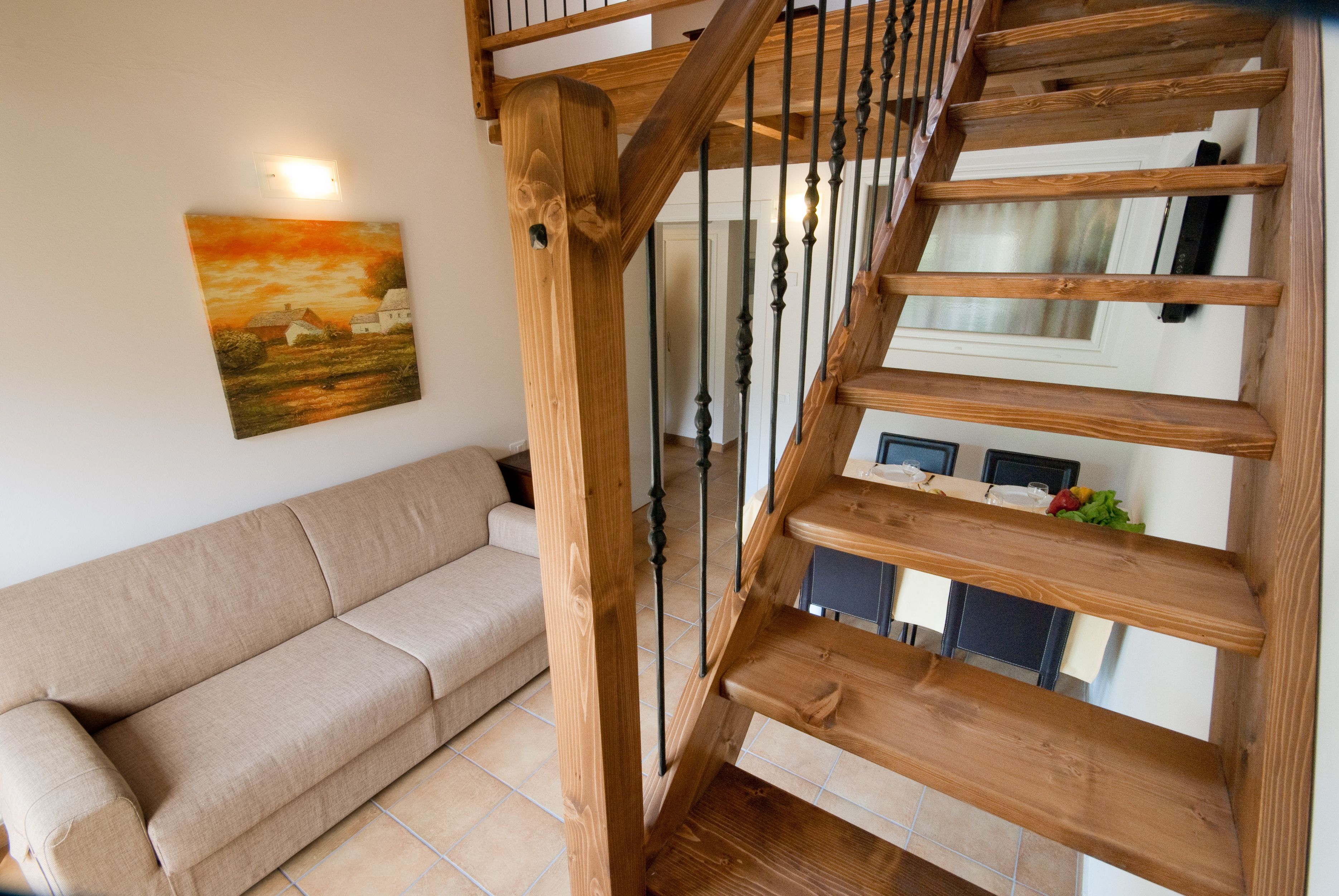 A wooden staircase with a handrail, a beige sofa, and a painting on the wall.