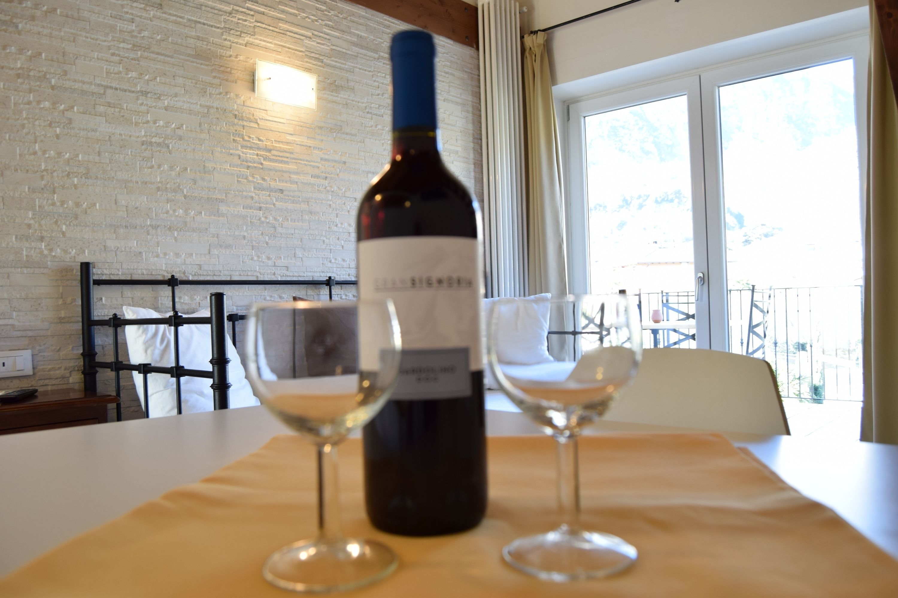 A bottle of wine and two glasses on a table in a room with a brick wall and a window.