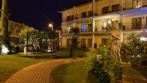 A hotel courtyard at night with a statue, a pool, and a well-maintained garden.
