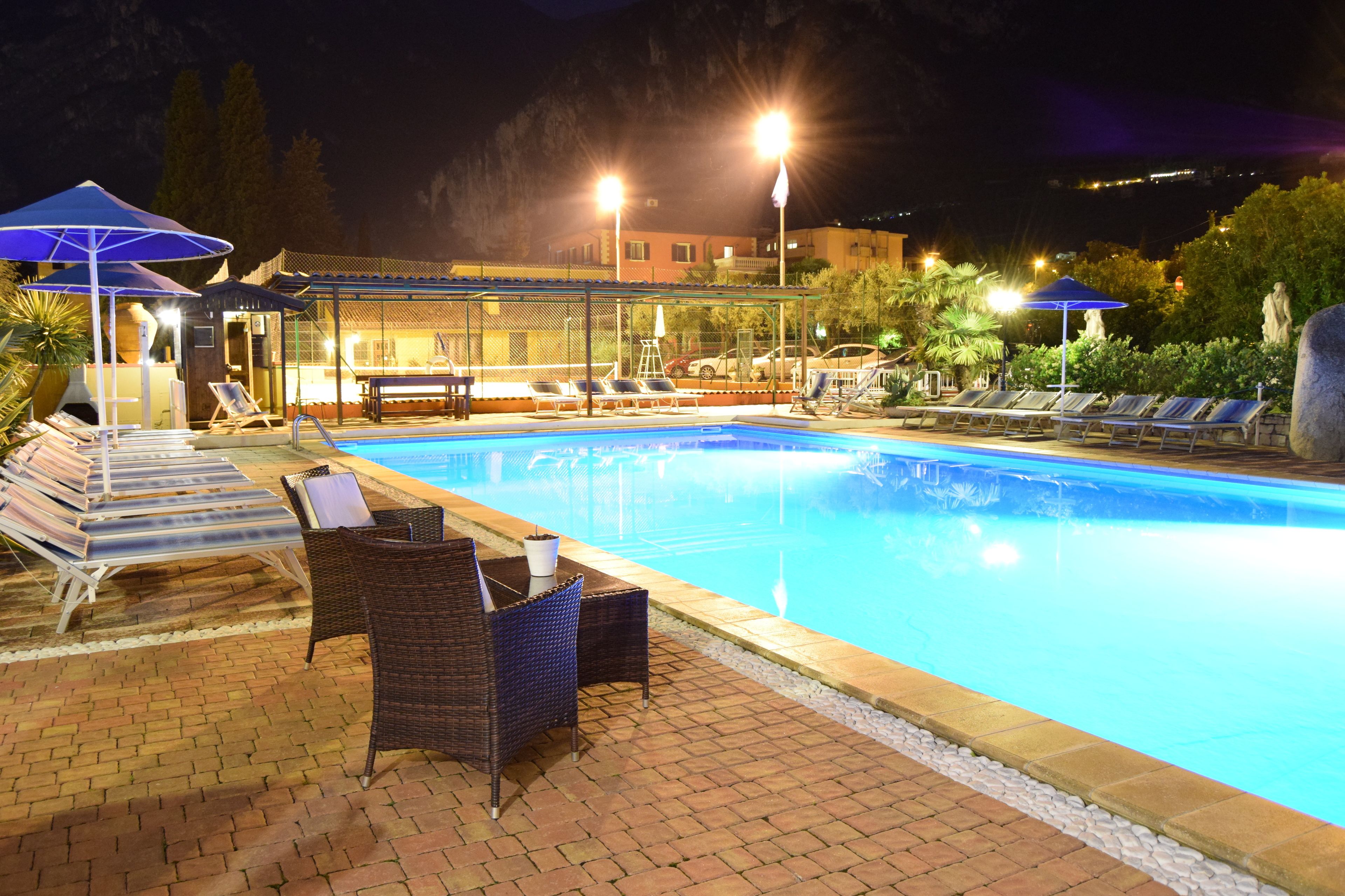 Ein Poolbereich bei Nacht mit Liegestühlen und Sonnenschirmen.
