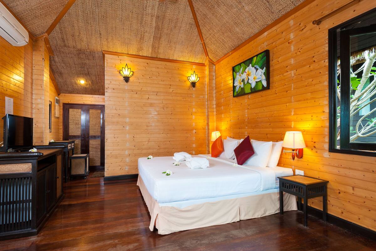 Ein Zimmer mit Holzboden, einem Bett, Nachttischlampen, einem Gemälde und einem Fernseher.