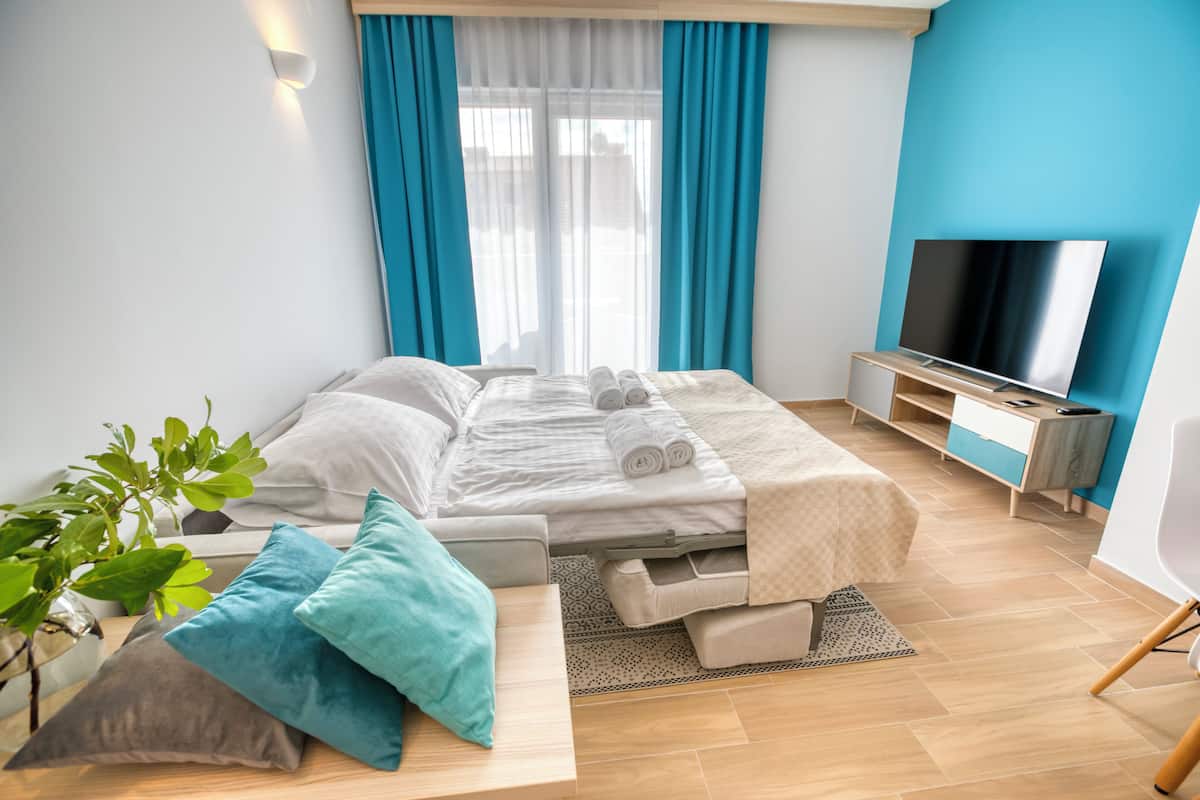 A modern hotel room with a bed, a TV, and a plant.