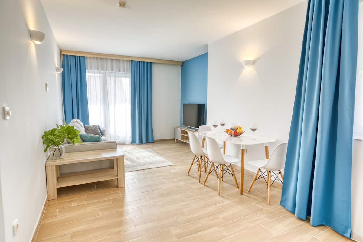A modern living room with a sofa, a coffee table, and a TV. There is a dining area with a table and chairs.