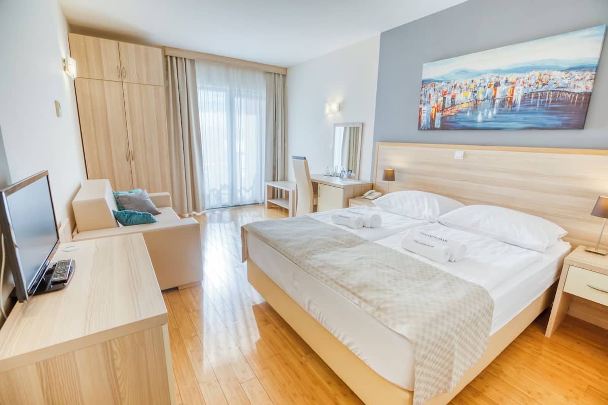 A hotel room with a bed, a desk, a chair, a TV, and a painting on the wall.