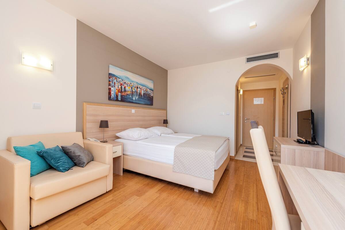A modern hotel room with a bed, a sofa, a desk, and a television.