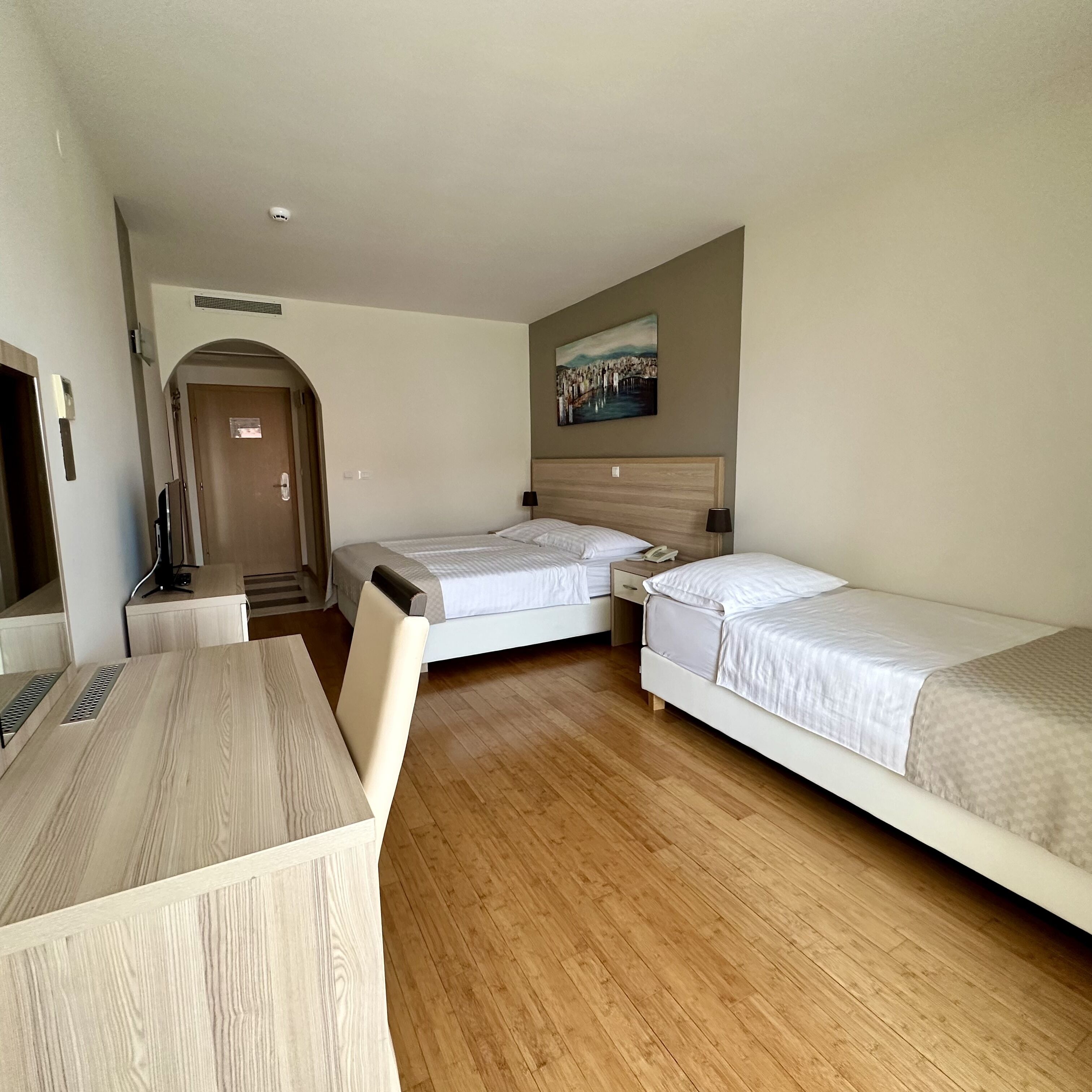 A hotel room with two single beds, a wooden desk, a chair, a TV, and a painting on the wall.