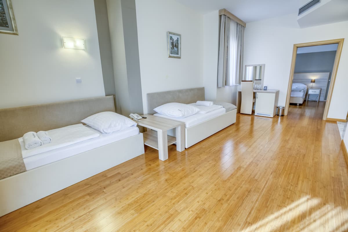 A hotel room with two single beds, a small bedside table, a desk, and a chair.