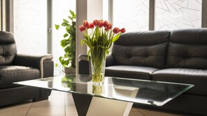 A modern living room with a glass coffee table, a vase of red tulips, and a black leather sofa. - Hotel Eiffel XV (Paris)