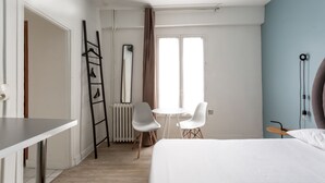 A bedroom with a bed, a desk, two chairs, a radiator, and a window. - Hotel Eiffel XV (Paris)