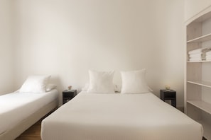 Ein schlicht eingerichtetes Schlafzimmer mit zwei Einzelbetten, jeweils mit weißen Bettwäsche und Kissen, sowie einem Nachttisch mit einer kleinen Blumenvase.